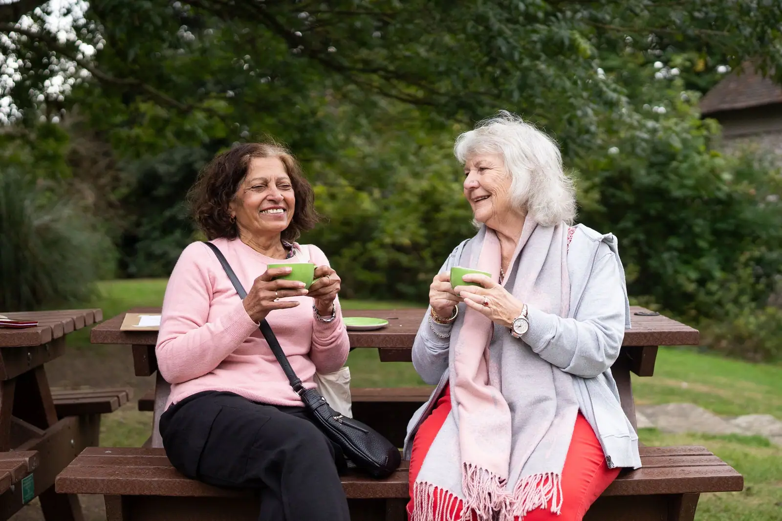 Two friends laughing together at the picnic table in the cottage garden
