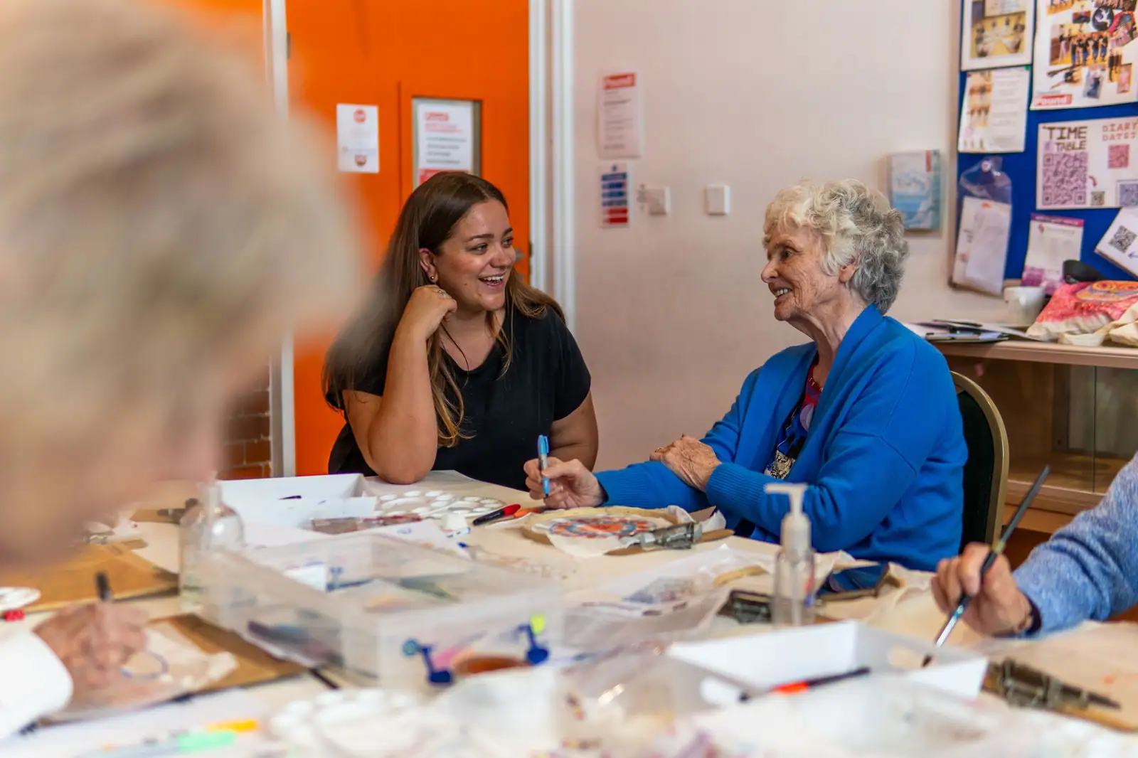 Members laughing together around the art studio table during a painting workshop