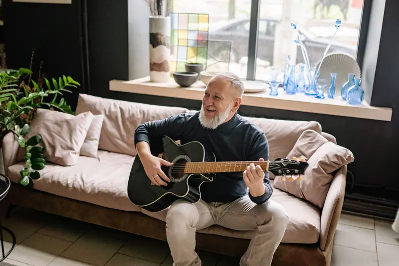 A grandfather playing guitar on the living room sofa