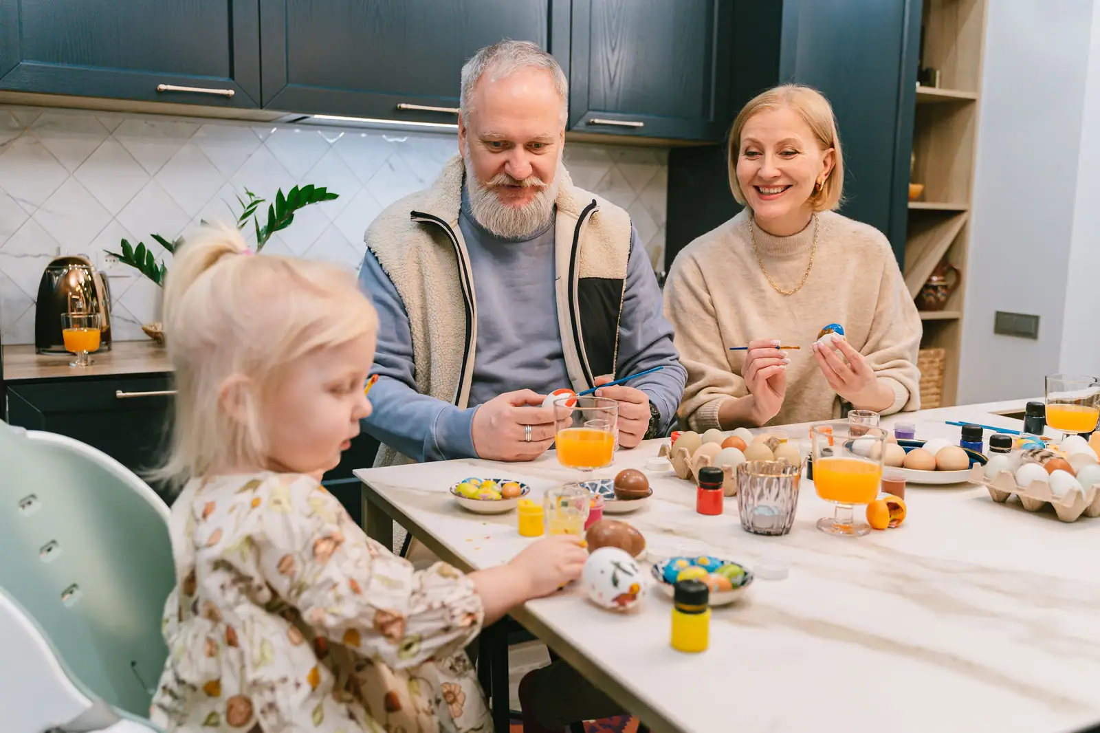 Three generations enjoying easter egg painting together in a cozy kitchen setting.