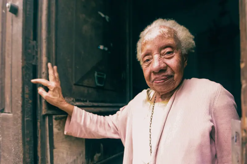 A smiling resident in a pink cardigan opening the old front door of the house