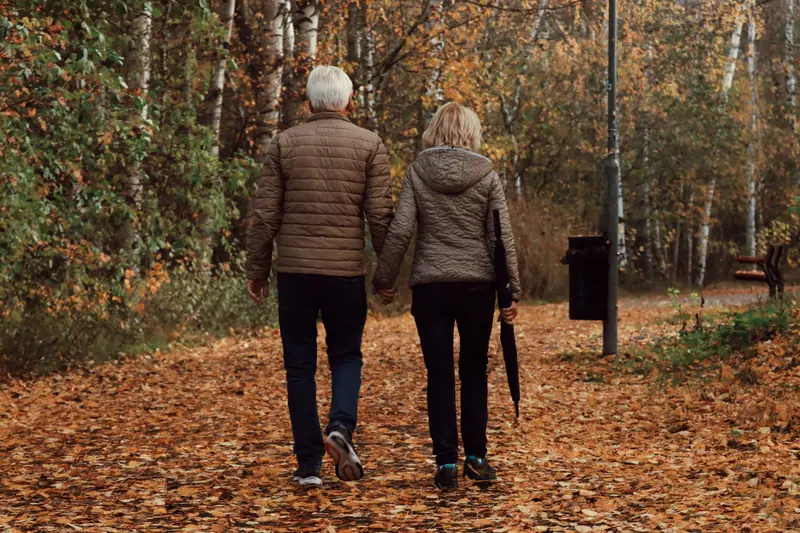 A couple walking arm in arm along a leaf-covered path