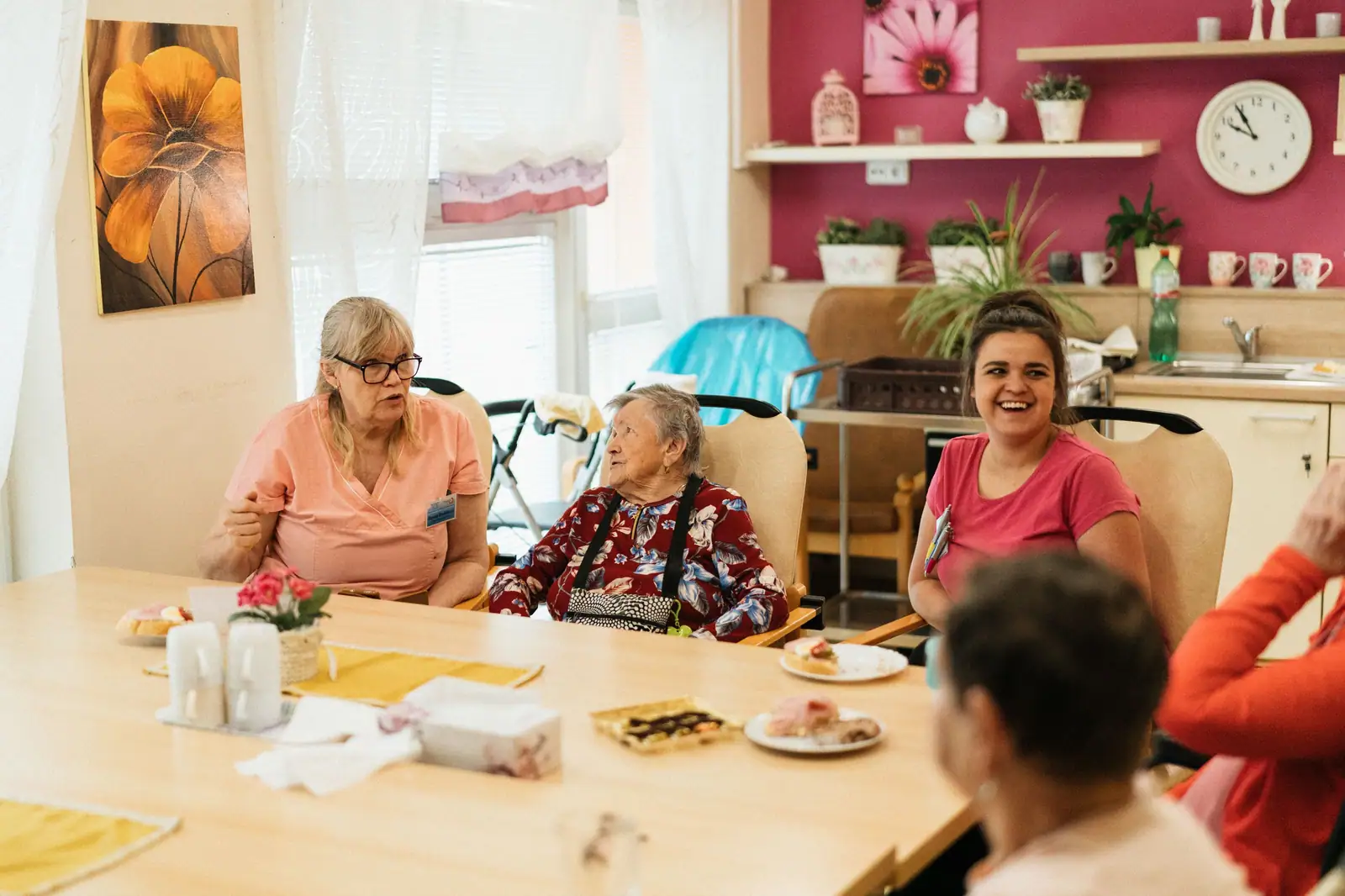 Residents and an aide laughing over coffee and pastries at the dayroom table