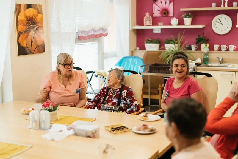 Residents and an aide laughing over coffee and pastries at the dayroom table