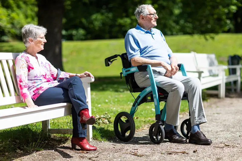 Two residents chatting on a garden bench, one resting beside his rollator