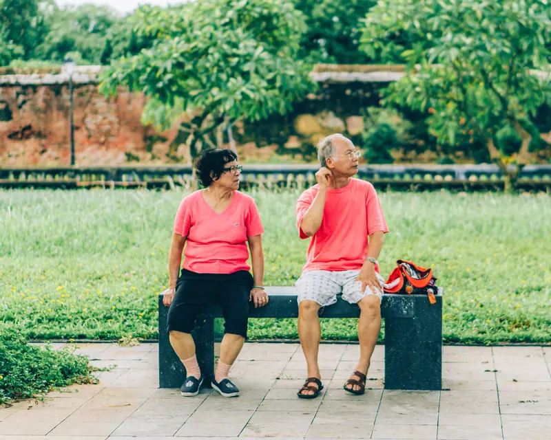 Two friends in matching red shirts chatting on a bench by the garden