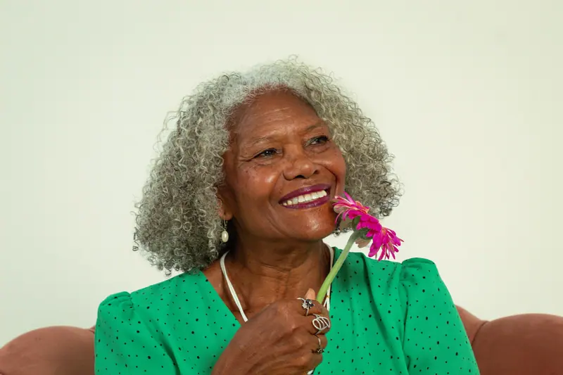 A smiling resident in a green dress holding a pink gerbera daisy
