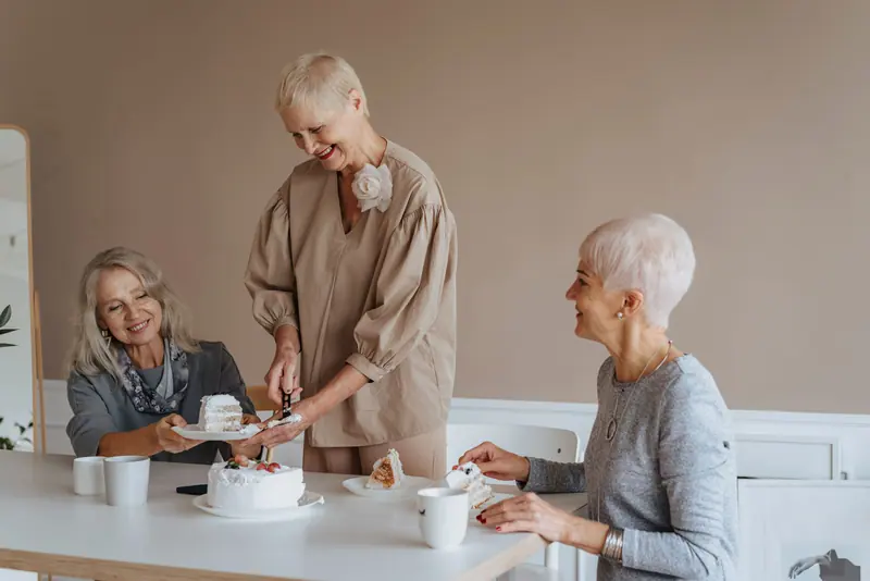 A caregiver cutting birthday cake for two residents