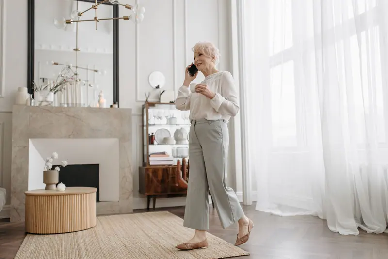 A resident on the phone in a white sitting room with a marble fireplace