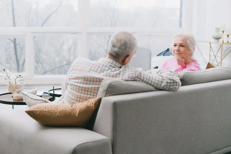 A couple talking on the sofa by the big windows
