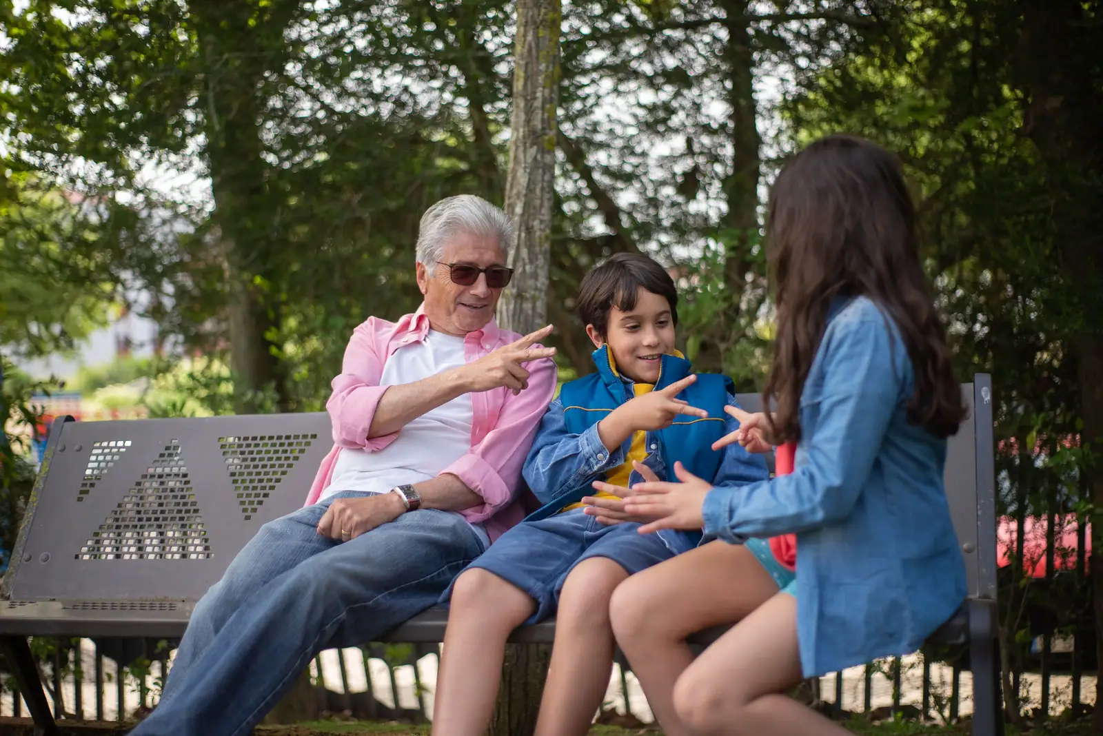 A resident playing rock-paper-scissors with his grandchildren on a park bench
