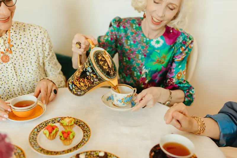 Friends pouring tea from a painted pot at a round table