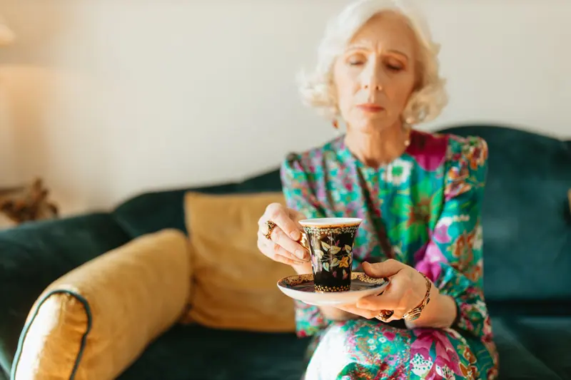 A resident with a china cup on the green velvet sofa