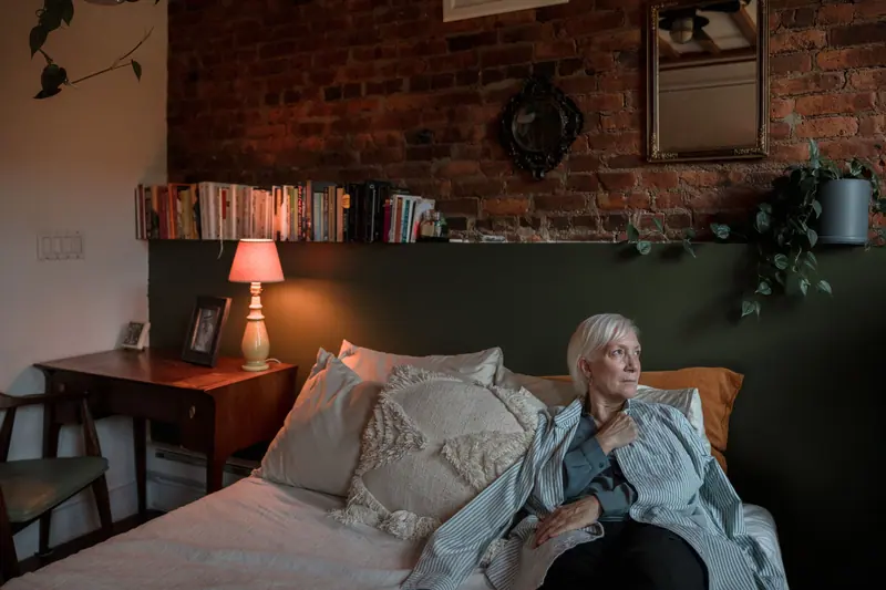 A resident resting against her pillows under a pink lamp in her apartment