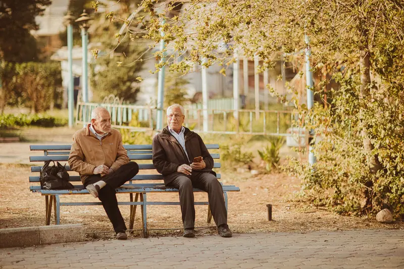 Two friends talking on a bench in the autumn sun