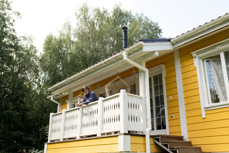 A resident waving from the porch of a yellow garden cottage