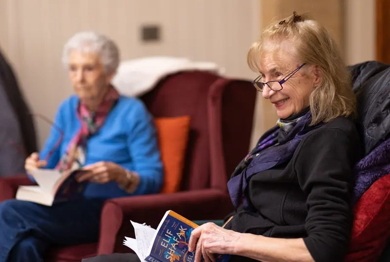 Two friends reading together in the library armchairs