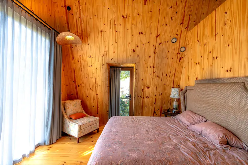 A charming bedroom with wooden paneling, armchair, and ambient natural light.