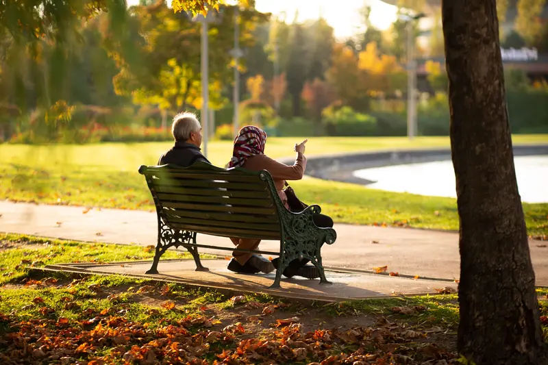 Two residents sharing a bench along the walking path in autumn