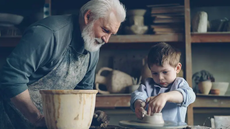 A grandfather teaching his grandson at the pottery wheel