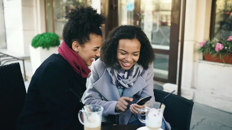 Two friends laughing over coffee at an outdoor table