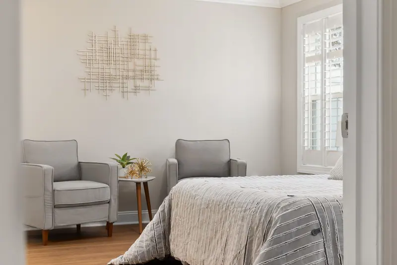 A bright, modern bedroom with grey armchairs and a stylish bed. Perfect for design inspiration.
