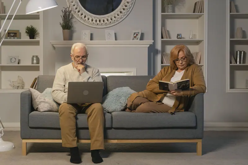 A couple relaxing on the sofa with a book and a laptop