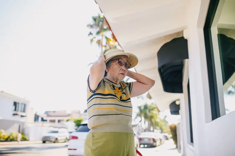 A resident adjusting her hat on the sidewalk