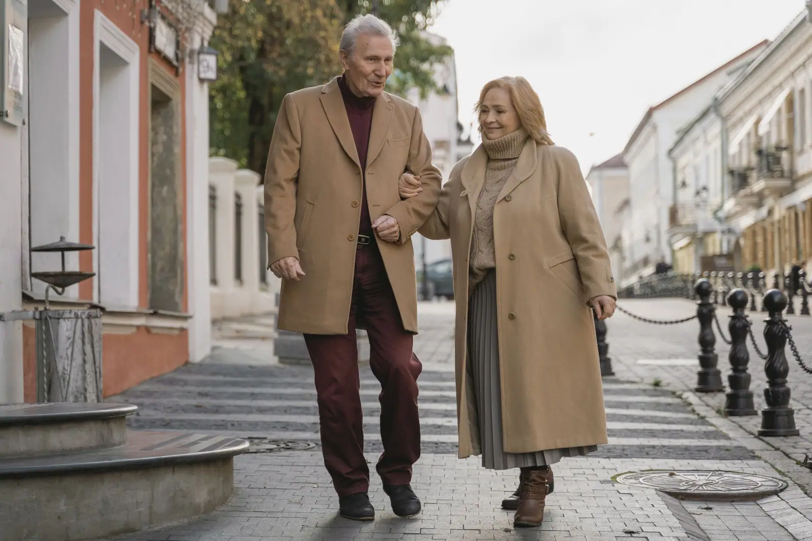 A husband and wife walking arm in arm down a city sidewalk in their winter coats