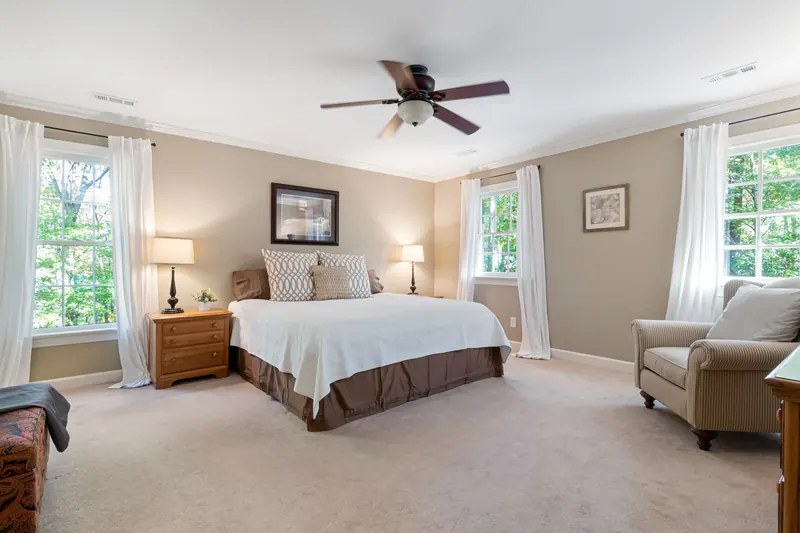 Bright and elegant bedroom interior featuring a bed and armchair with natural lighting through large windows.