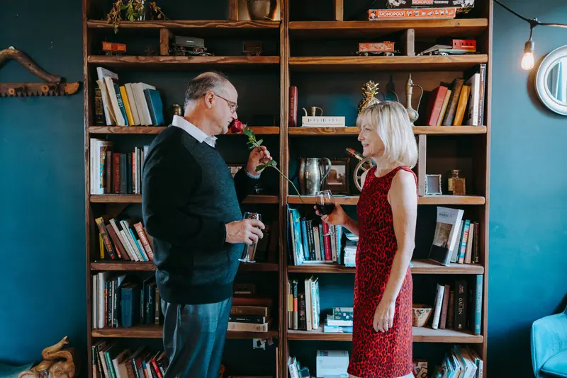 A wife handing her husband a rose among the bookshelves of their living room