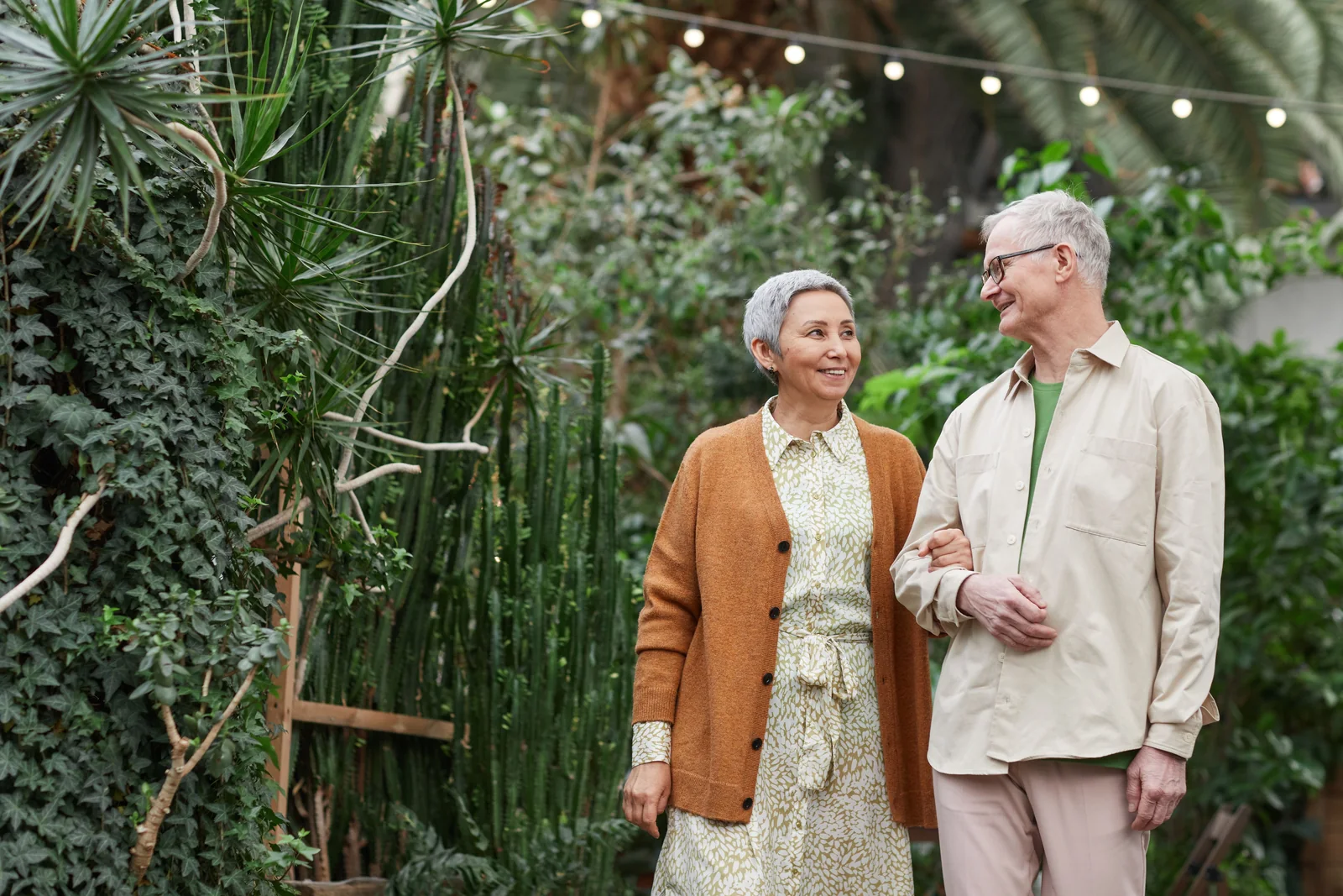 An older couple strolling arm in arm through a garden conservatory