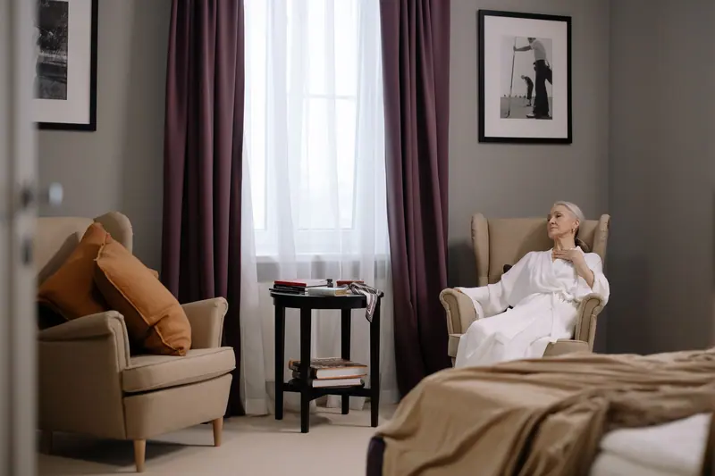 Senior woman in a comfortable bedroom, sitting in a chair and relaxing in a robe.