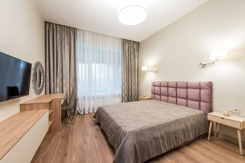 Spacious bedroom featuring modern furniture and neutral colors with natural light.