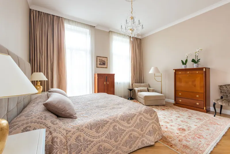 Spacious vintage-style bedroom featuring a soft color palette, chandelier, and classic furniture.