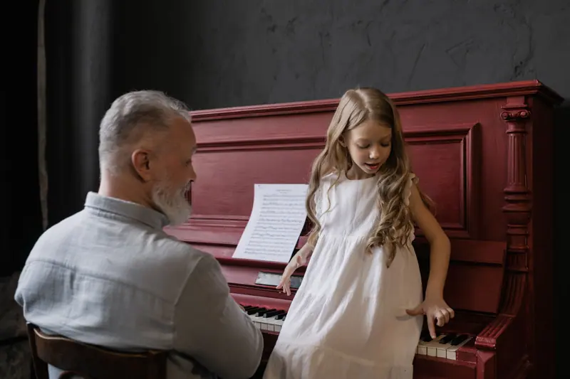 A grandfather teaching his granddaughter a tune at the piano