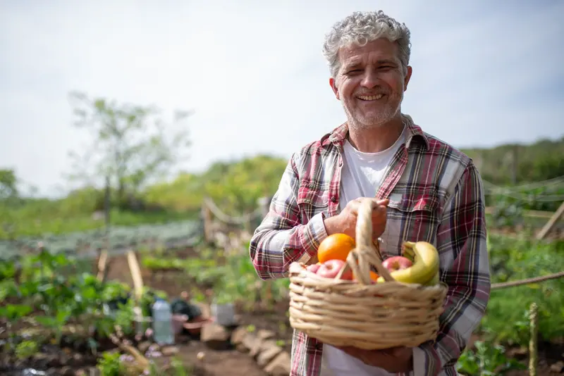 A resident holding a basket of peppers and tomatoes from the garden beds