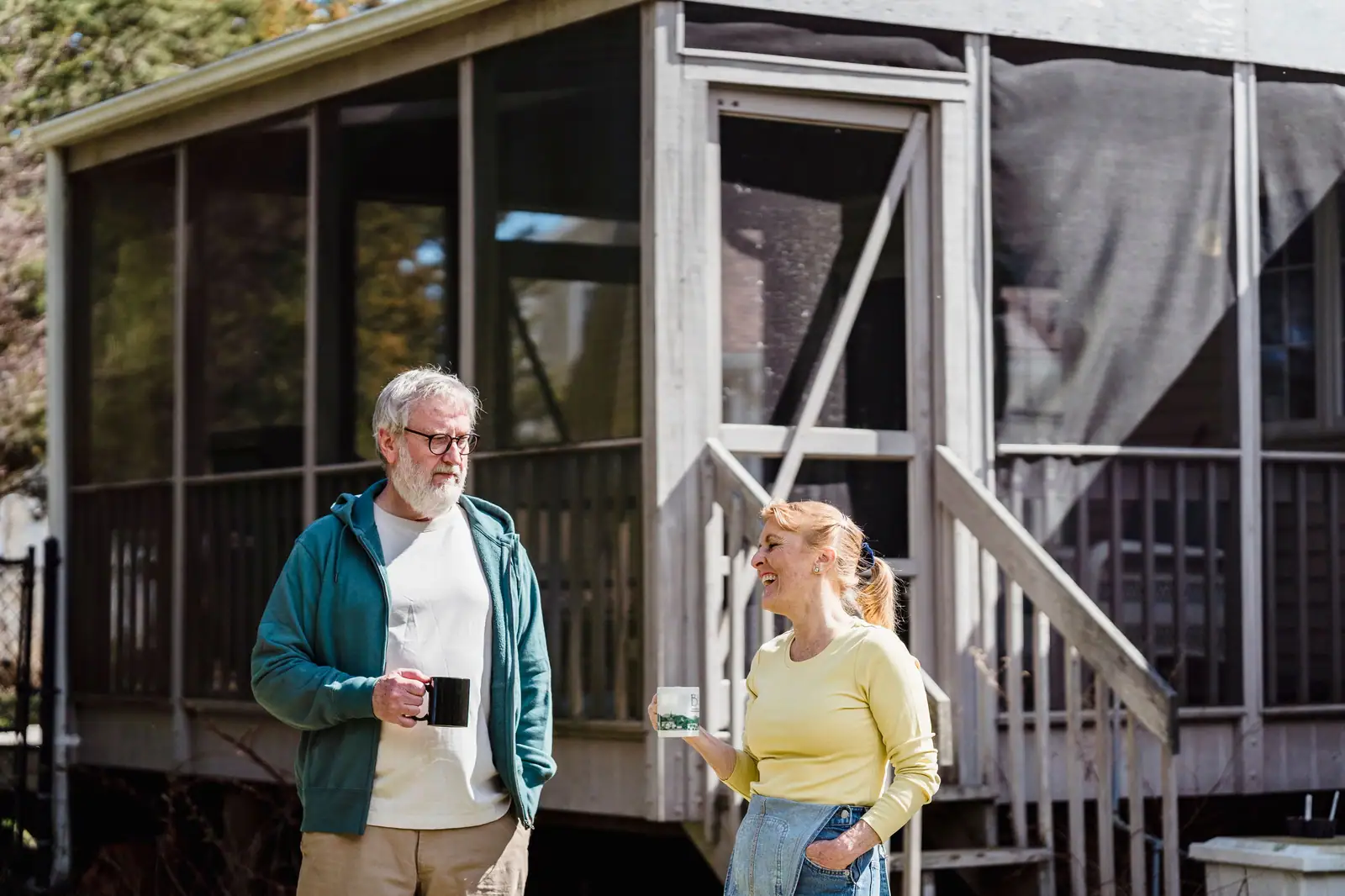 A couple chatting with their coffee outside their cottage screen porch