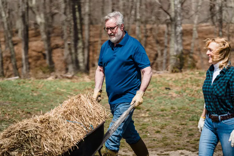 A resident hauling straw to the community garden beds while his wife looks on