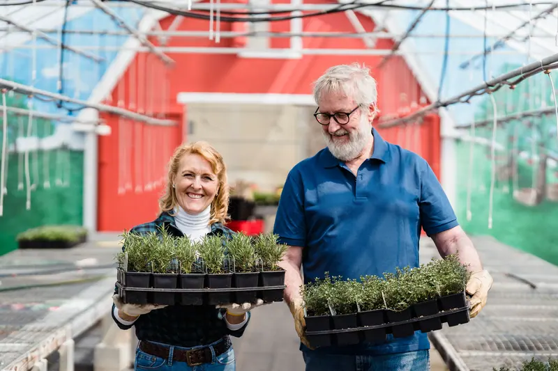 Two residents carrying seedlings out of the greenhouse