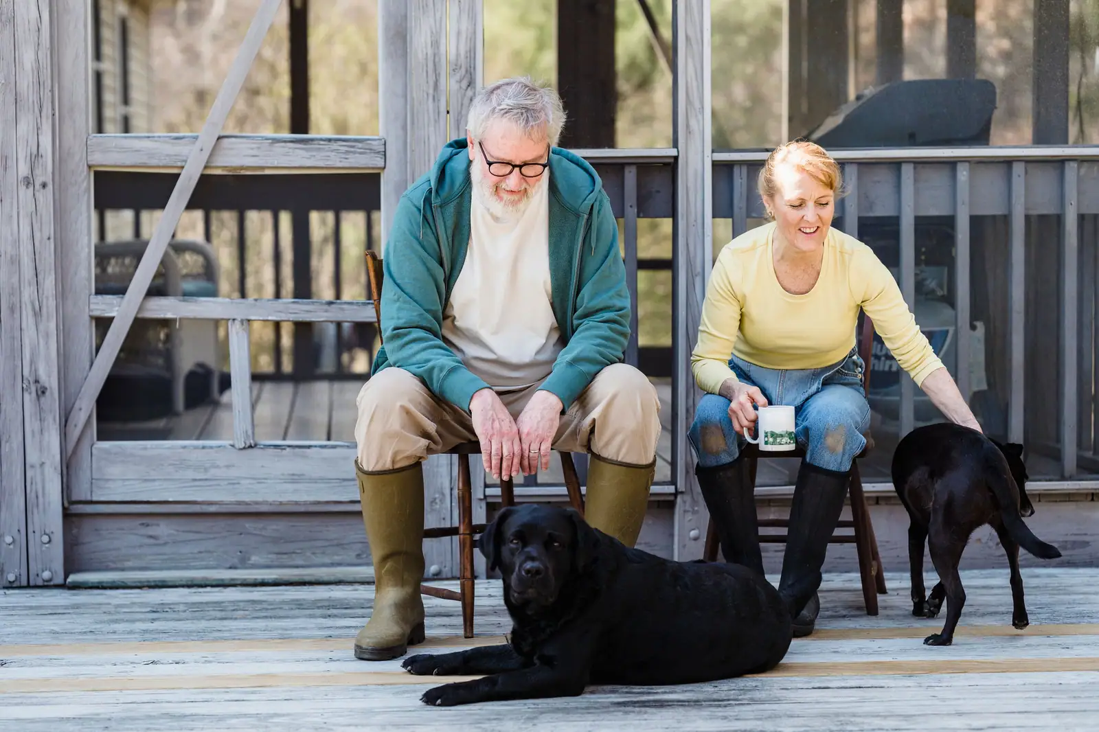 A couple relaxing on the porch of their cottage with their two black Labradors