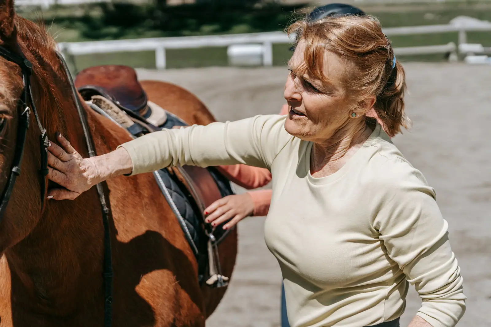 A resident saddling her chestnut horse in the arena on a clear morning