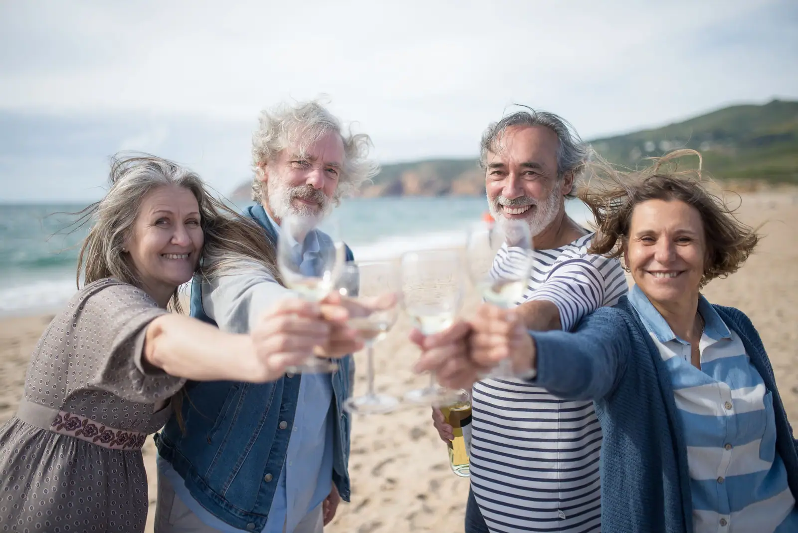 Four friends raising their glasses on the beach in their navy stripes