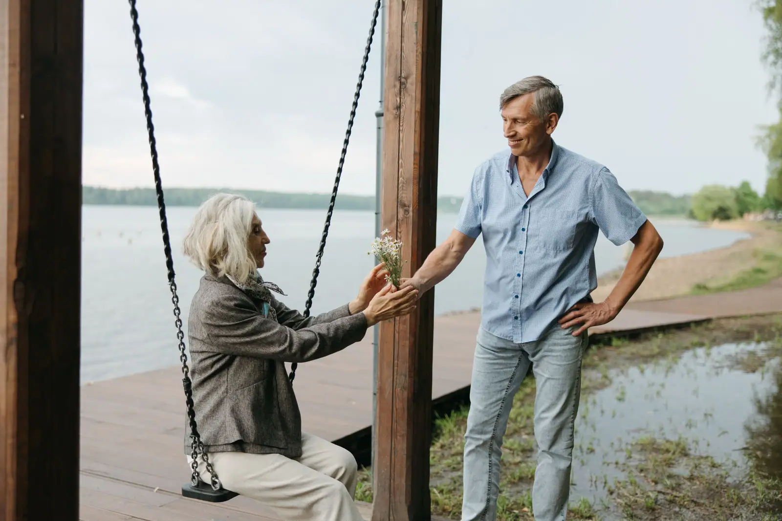 A husband and wife at the lake's edge, she on the shoreline swing and he leaning in beside her