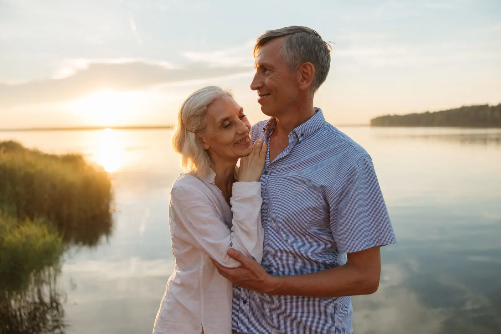 A husband and wife holding each other at the edge of the lake as the sun goes down