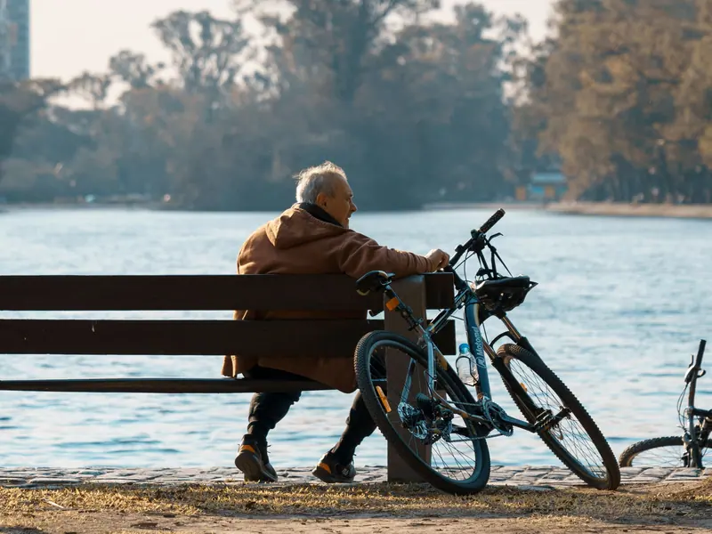 A resident resting on a bench by the water with his bicycle