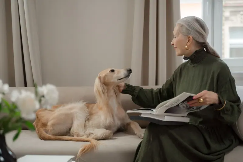 An older woman reading on the sofa with her dog