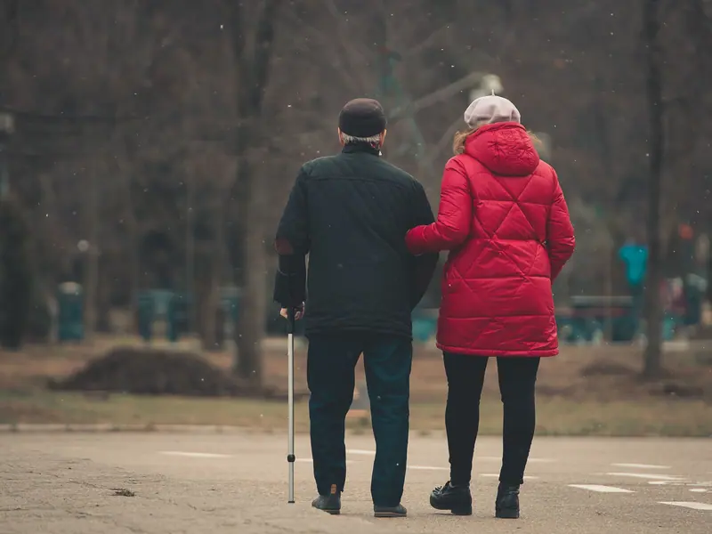 A couple walking arm in arm on an autumn afternoon, his cane in hand