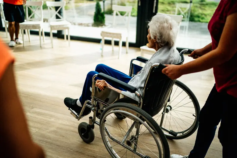 An aide wheeling a resident through the sunny day room