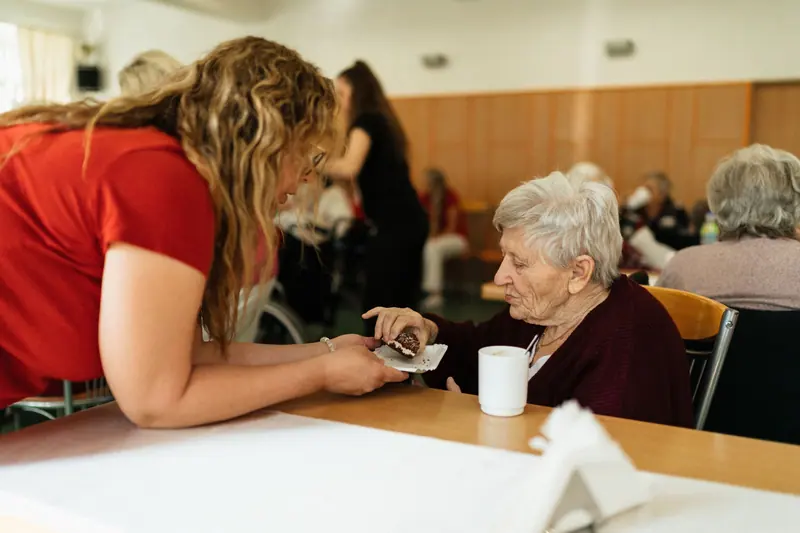 A nurse leaning in to help a resident at the dining table